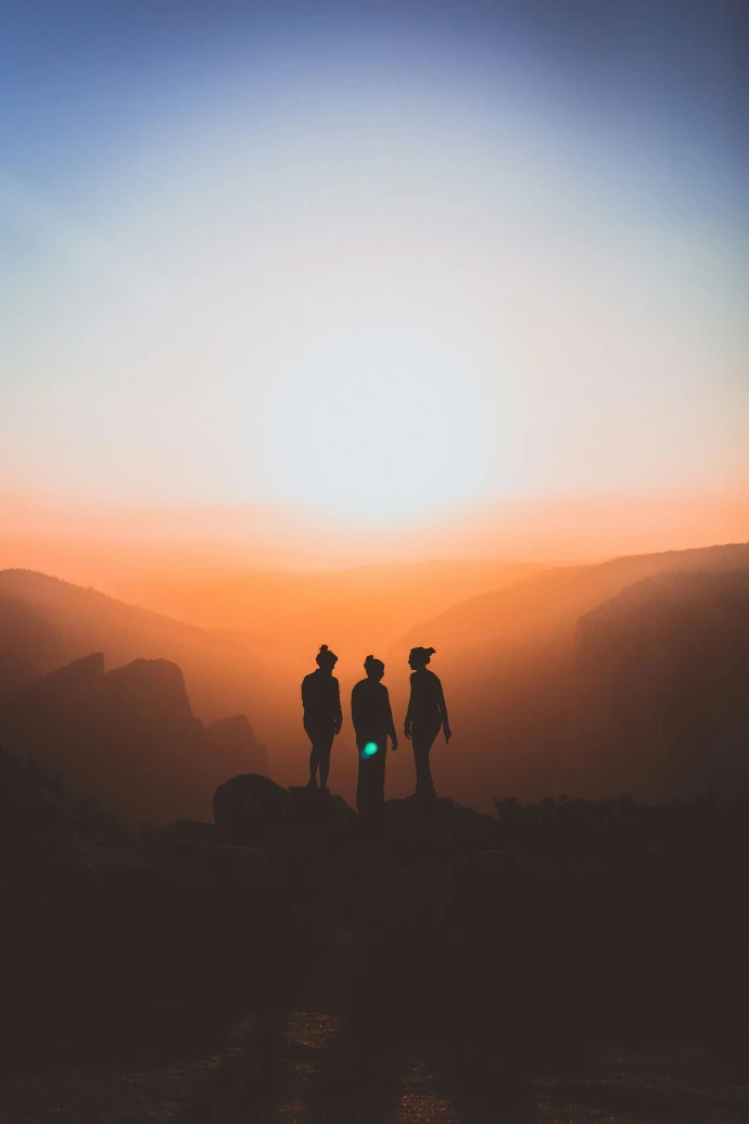 silhouette of three people up on mountain cliff